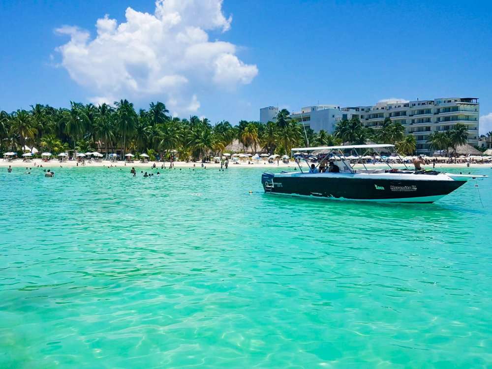 A boat floating on the water at Isla Mujeres Playa Norte with palm trees in the background