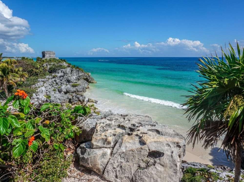 The Tulum Ruins overlooking the ocean with rocks and palm trees