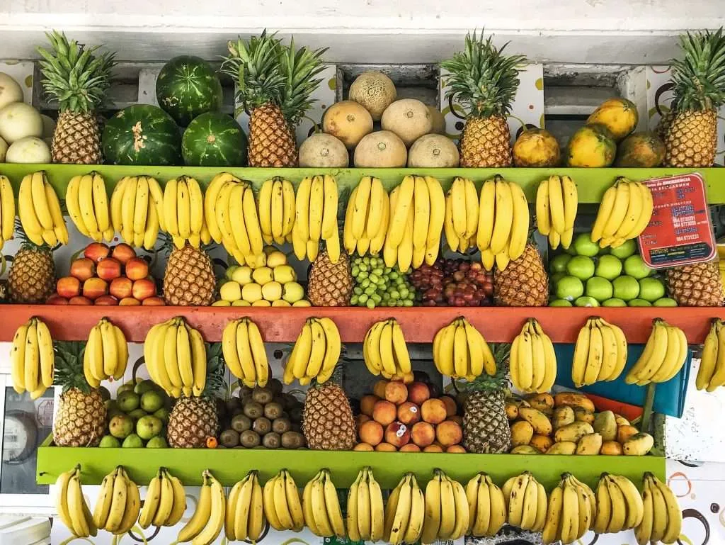 A fruit stand in Playa del Carmen with hanging bananas, pineapples, and fresh fruits