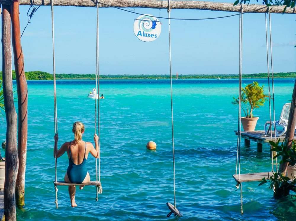 A girl on a wooden swing over the water at Bacalar Lagoon Mexico