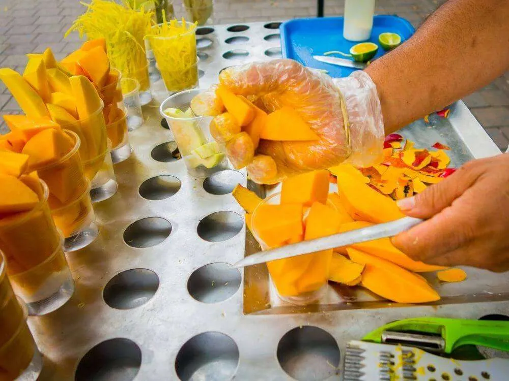 A person cutting up slices of mangos, a popular street food in Playa del Carmen