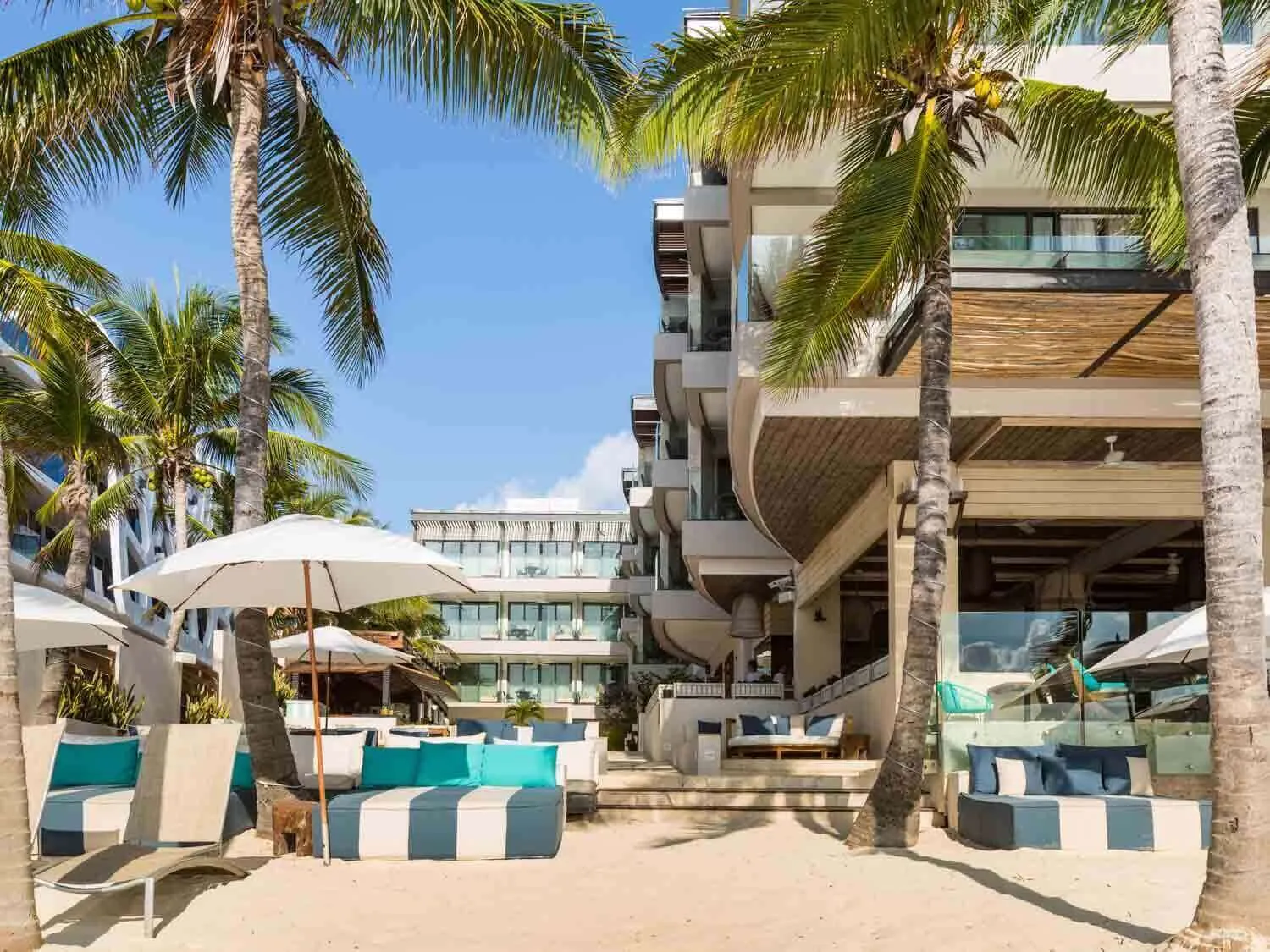 The beachfront area at Thompson Beach House Playa del Carmen Boutique Hotel with lounge beds and palm trees