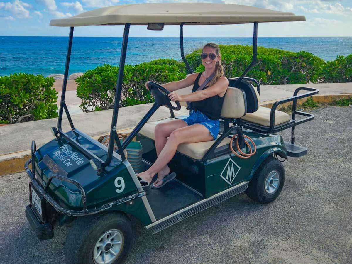 Me driving a golf cart along a coastal path on a day trip to Isla Mujeres with the ocean and tropical bushes in the background