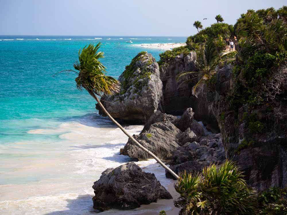 The beach at the Tulum Ruins with turquoise water and cliffs with palm trees