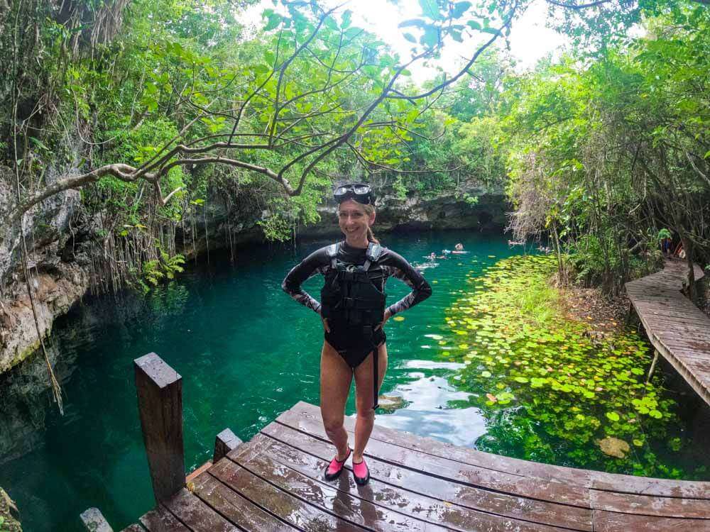 Me standing in front of a cenote on the Xenotes tour surrounded by trees