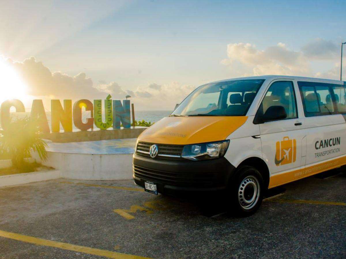 A Cancun Airport Transportation Van parked next to the Cancun sign