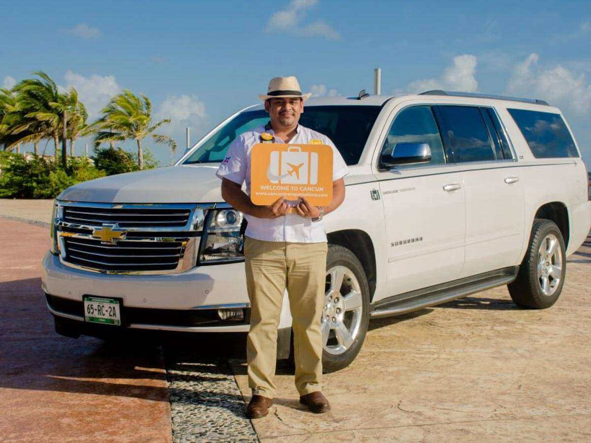 A driver standing in front of a luxury Cancun Airport transportation SUV