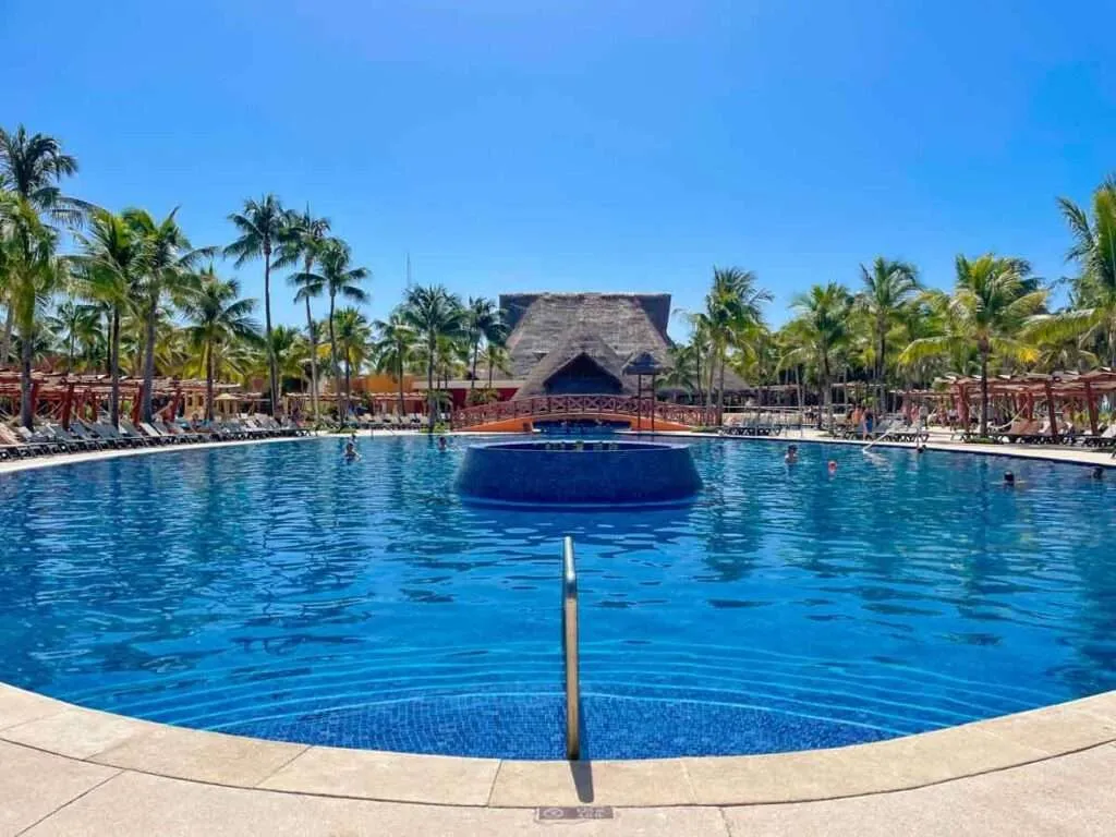 A circular pool surrounded by lounge chairs and palm trees at Barcelo Maya Colonial resort