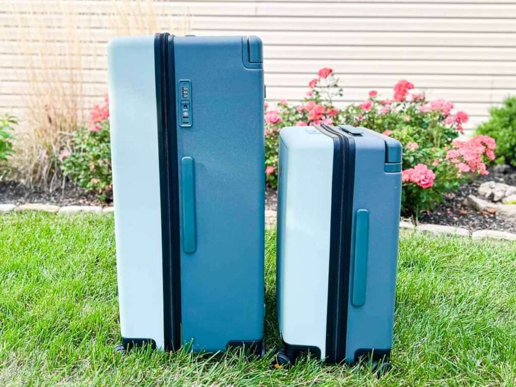 A Side-By-Side Comparison of the Level8 Voyageur Checked 28" Luggage and the Level8 Voyageur Carry-On on the grass with pink flowers in the background