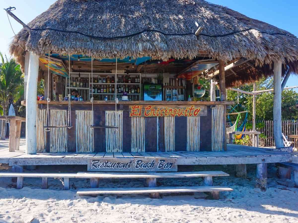 A beach bar in Holbox Mexico with a thatched roof and swings