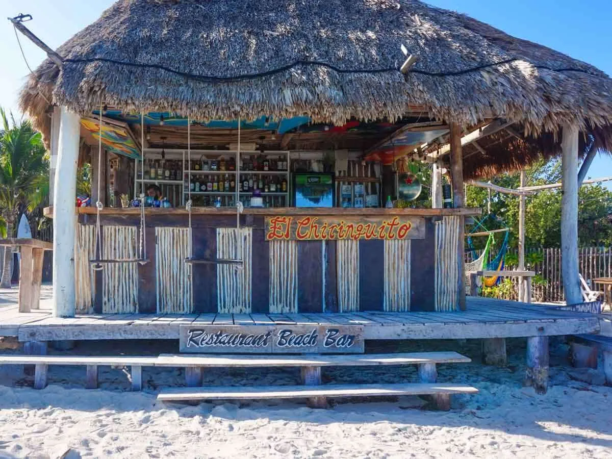 A beach bar in Holbox Mexico with a thatched roof and swings