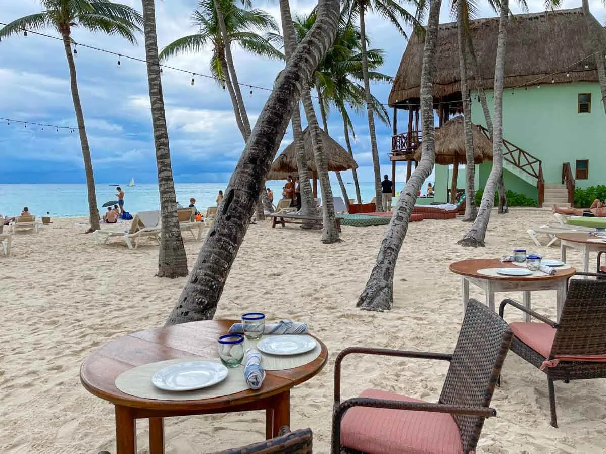 Tables and chairs on the beach surrounded by palm trees at Fuego Restaurant Playa del Carmen