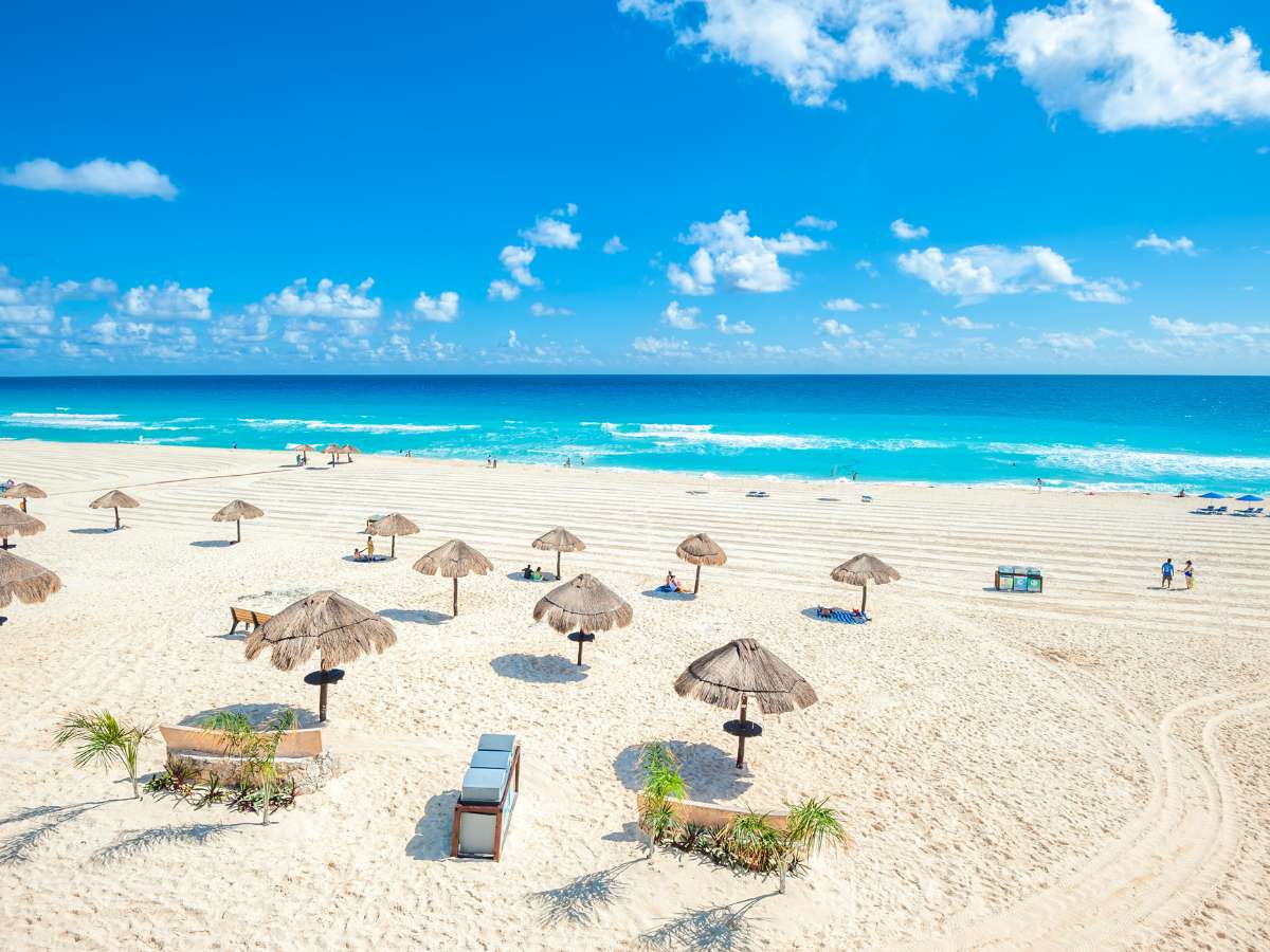 A beach in Cancun Mexico with thatched umbrellas