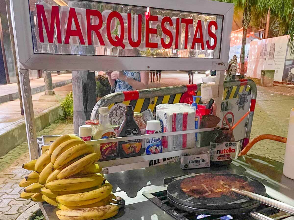 A marquesitas cart with bananas and fillings next to a hot plate