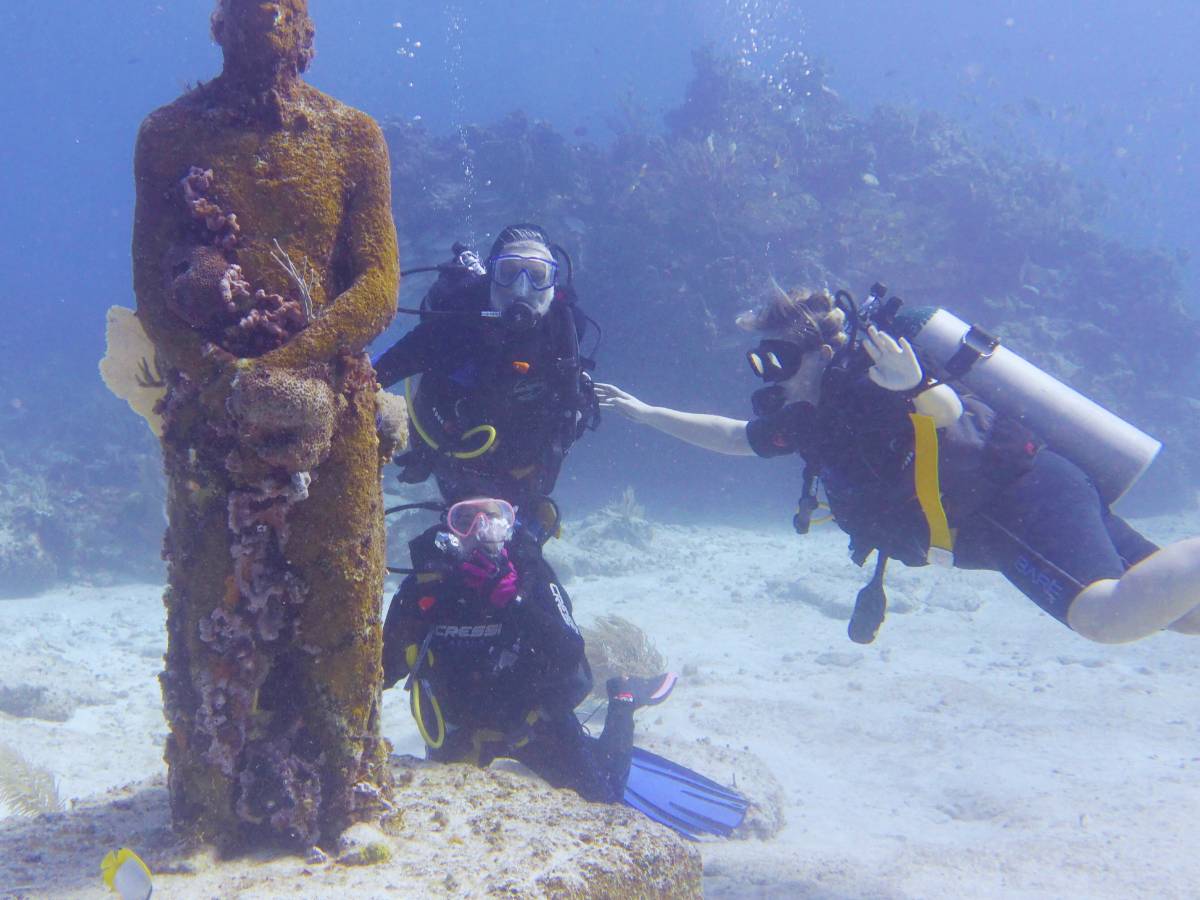 A group of people scuba diving next to a statue at the MUSA underwater museum of art