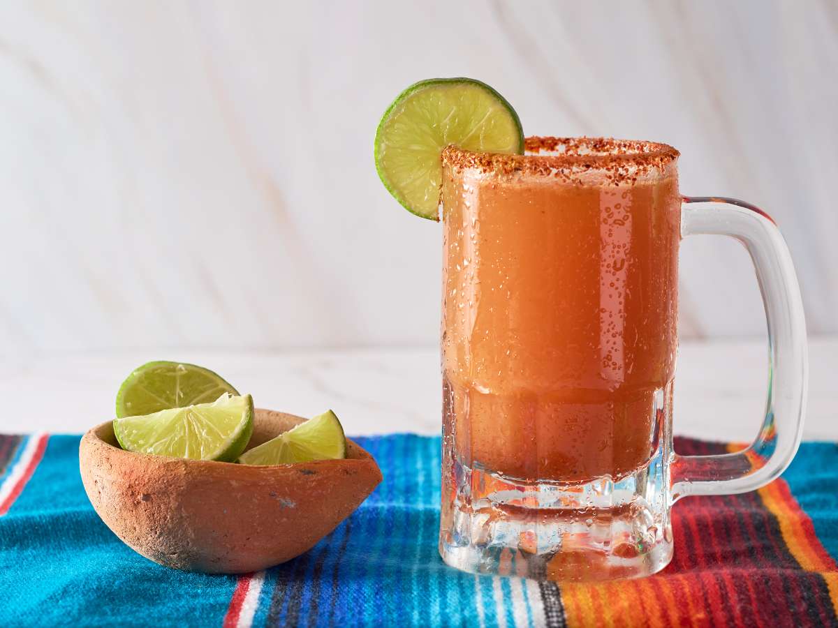 A glass mug of michelada next to a bowl of limes